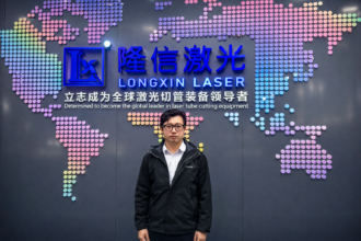 Eric Yueng at Longxin Laser headquarters in front of the company’s laser tube cutting and AI SmartCut branding