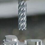 High-precision CNC end mill positioned above a machined aluminium component inside a modern industrial environment