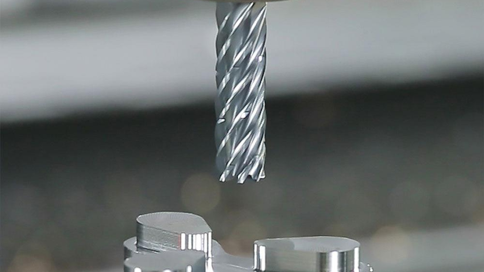 High-precision CNC end mill positioned above a machined aluminium component inside a modern industrial environment