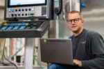 Zimmermann engineer using laptop beside CNC control system for cyber resilience digital twin AI and high precision portal milling machine development