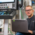 Zimmermann engineer using laptop beside CNC control system for cyber resilience digital twin AI and high precision portal milling machine development