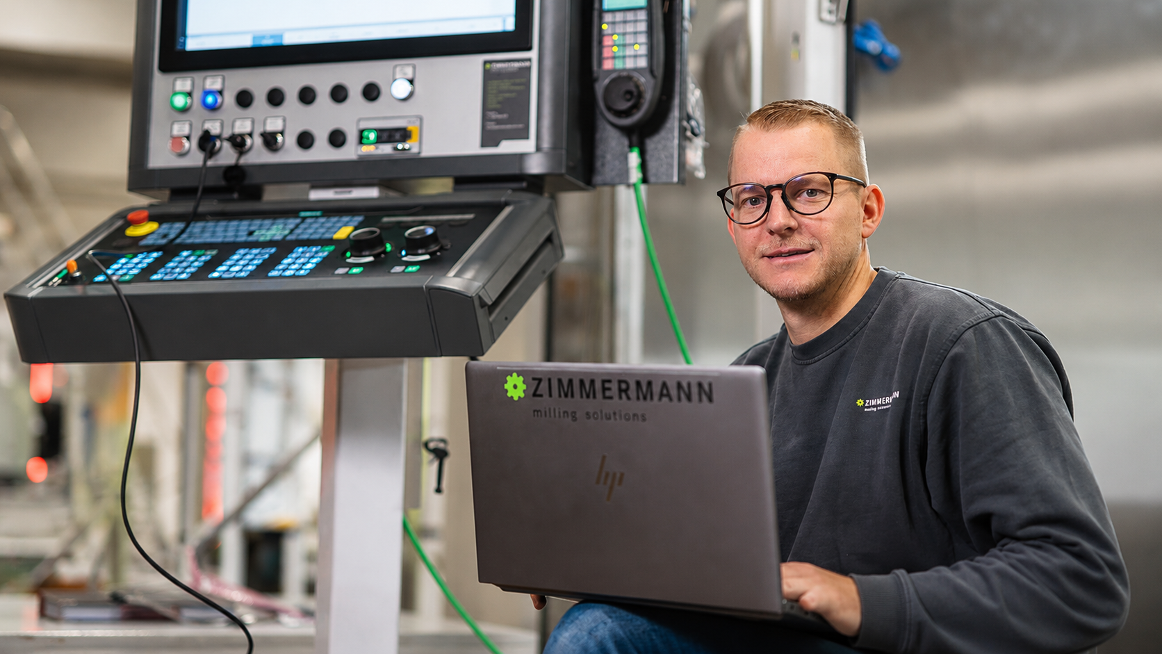 Zimmermann engineer using laptop beside CNC control system for cyber resilience digital twin AI and high precision portal milling machine development