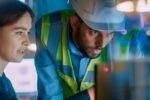 Hexagon report on AI in manufacturing: a woman and a man wearing a hard hat review a screen on the factory floor.