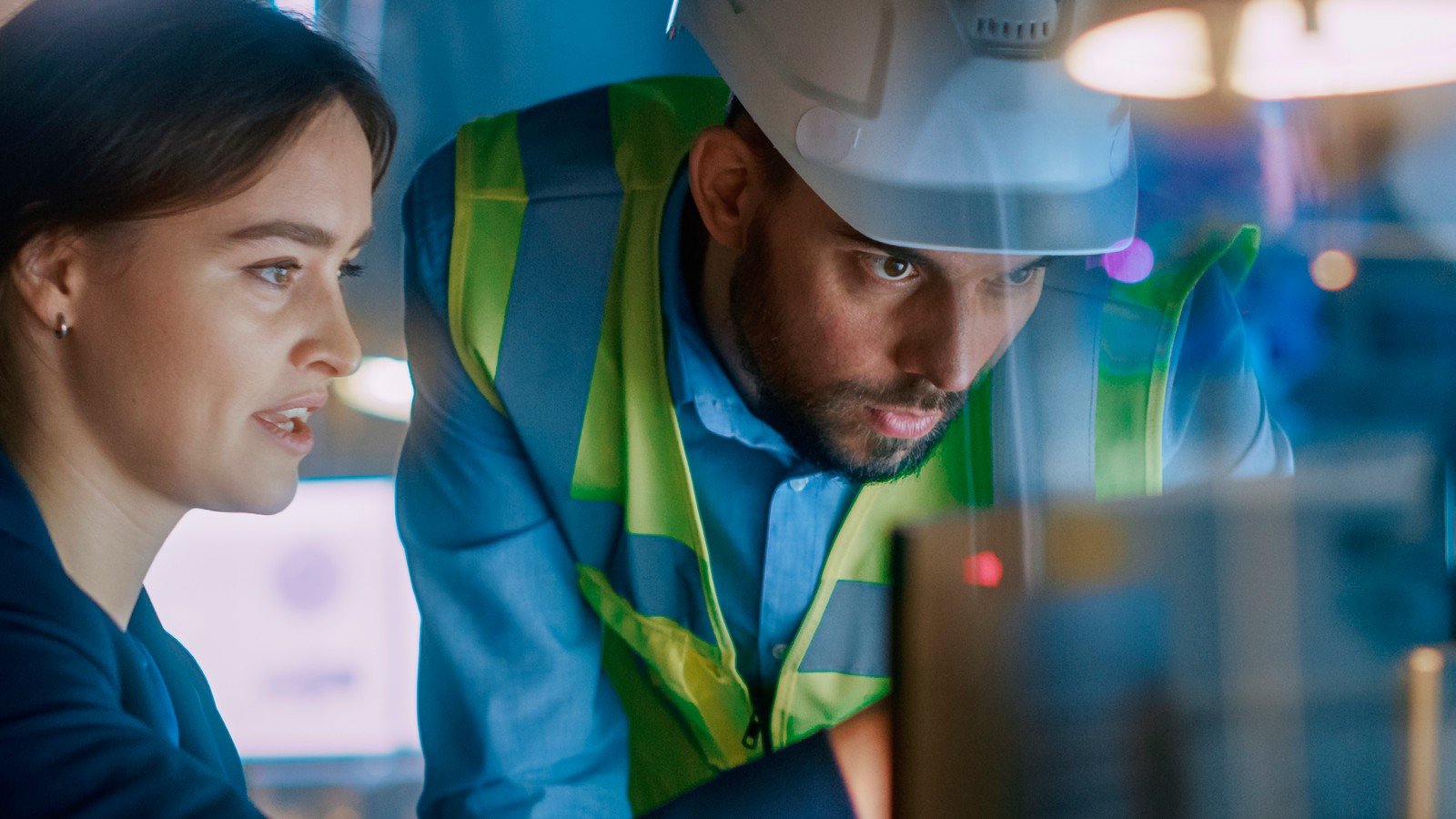 Hexagon report on AI in manufacturing: a woman and a man wearing a hard hat review a screen on the factory floor.